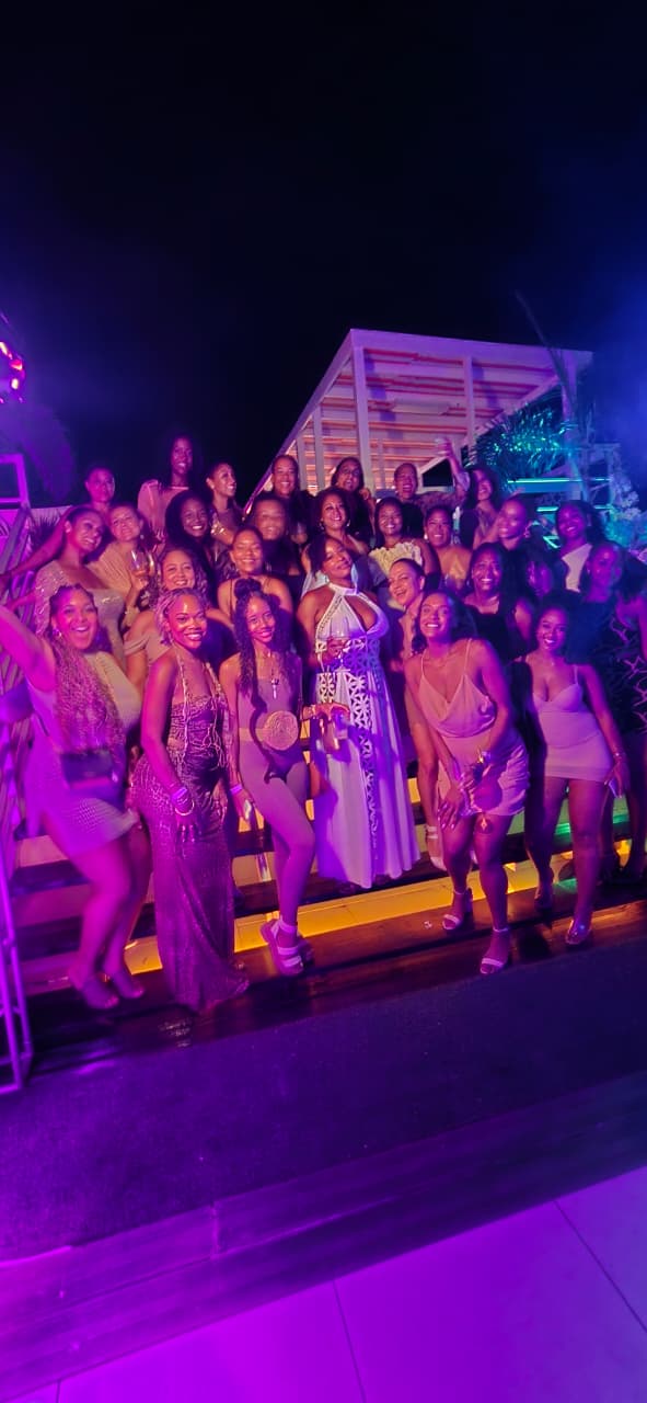 A big dressed-up crew posing together on lit steps under purple party lights at a Mowatt Tours night out in Jamaica