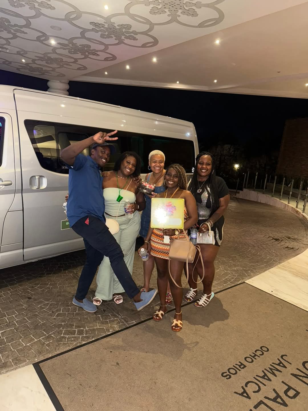 A dressed-up group of guests posing with their driver in front of the Mowatt Tours van under the hotel entrance lights at night