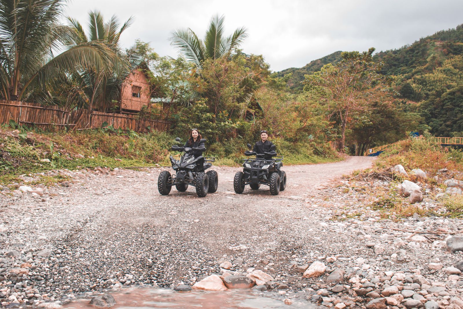 Two riders on four-wheelers splashing along a jungle trail