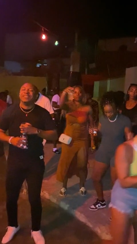 Friends with drinks dancing under string lights at a Jamaican street party